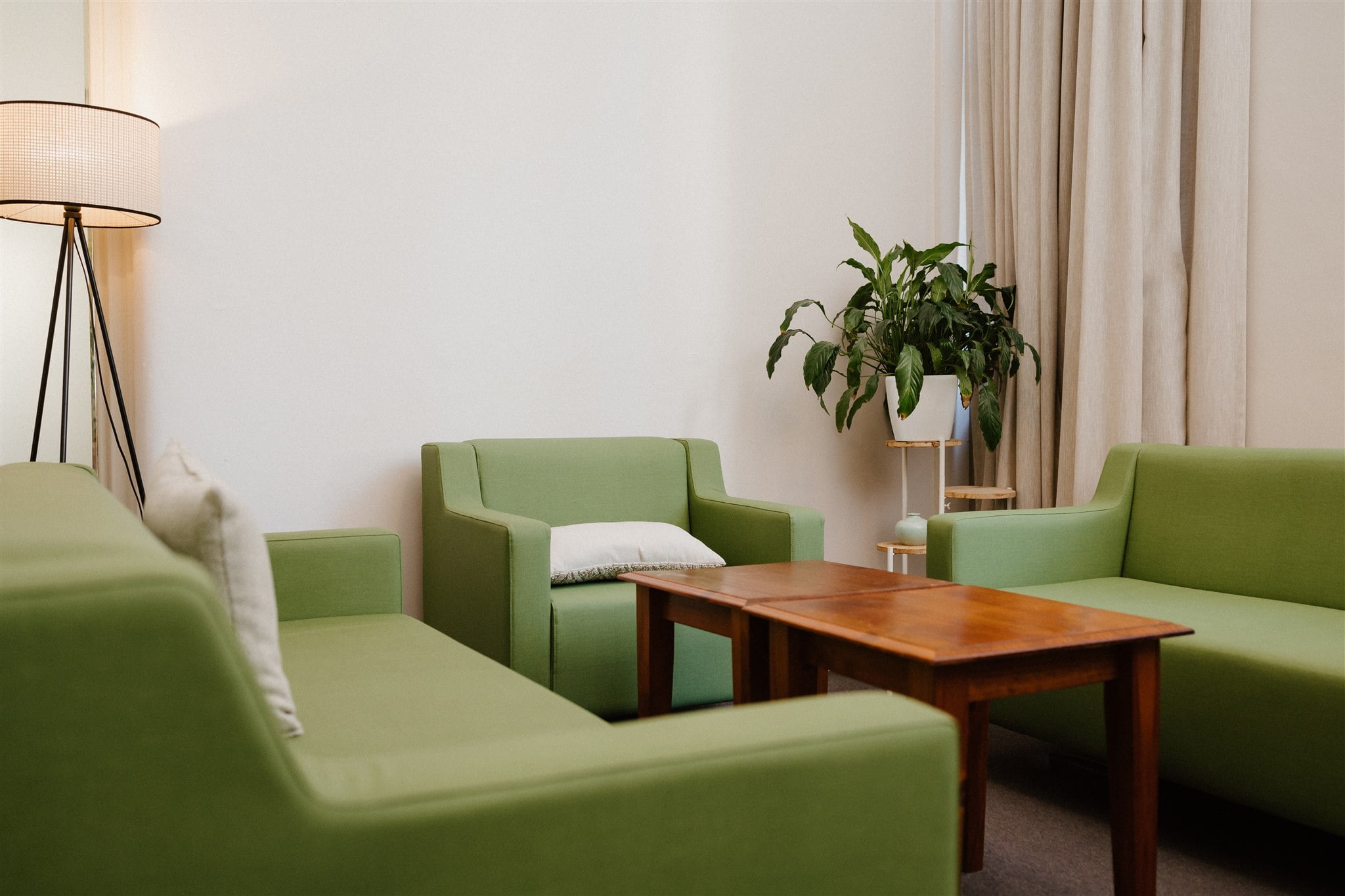 A counselling room with three green seats and couches around a table. Room decor includes a plant, lamp and cushions.